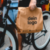 Person transportiert eine individuell bedruckbare Kraftpapier-Tragetasche auf einem Fahrrad